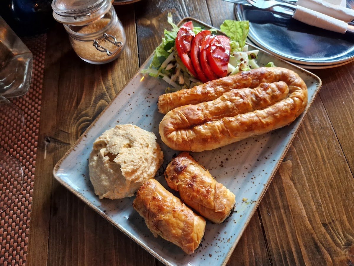 A long twisted börek, two golden pastry rolls, a scoop of hummus and a tomato and lettuce salad on a speckled blue platter.