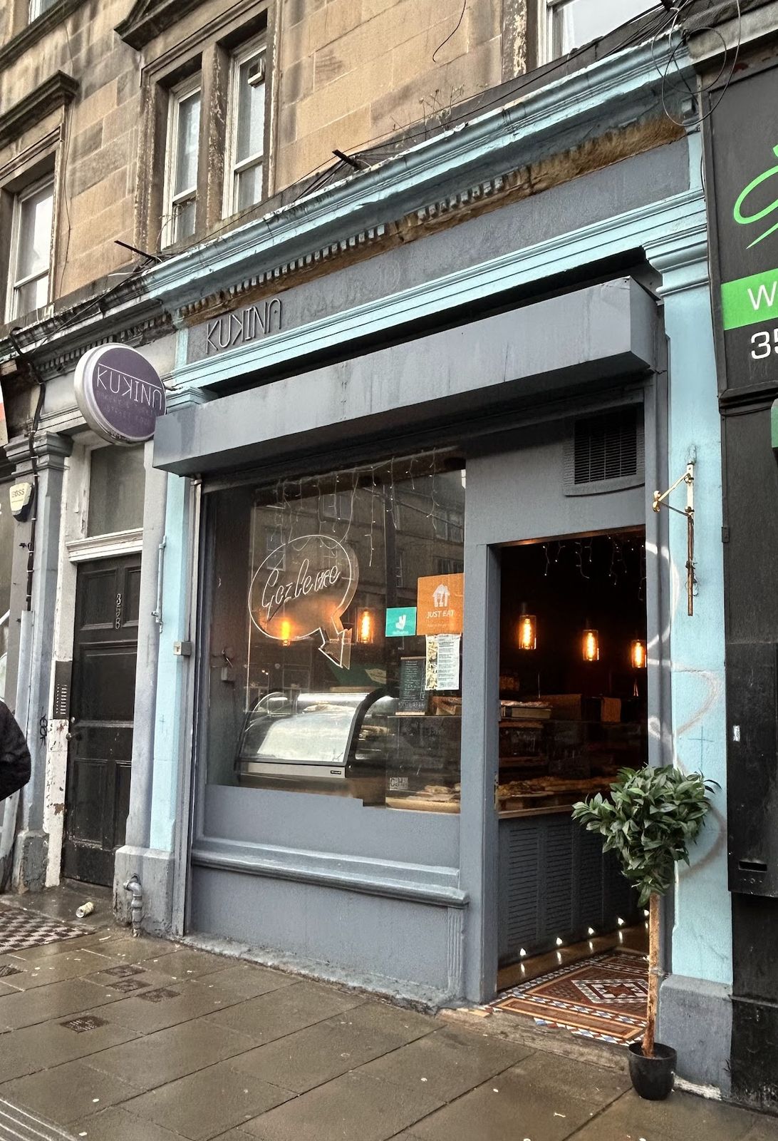 Kukina's pale blue-grey shopfront on Leith Walk, with a round KUKINA sign, a neon 'Gözleme' in the window and a potted bay tree by the open door.